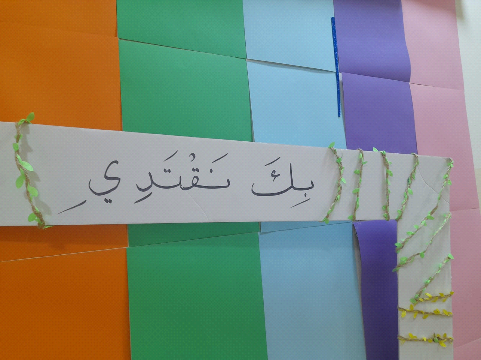 إطار يحمل عبارة 'بك نقتدي' مزين بأوراق شجر على خلفية ملونة